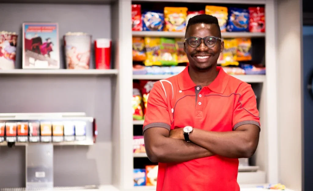 Smiling Product Promoter in red polo shirt, arms crossed, standing in store.